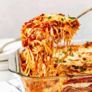Southern baked spaghetti in a casserole dish with a spoonful being lifted with a spoon.