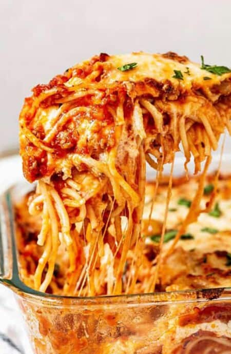 Southern baked spaghetti in a casserole dish with a spoonful being lifted with a spoon.