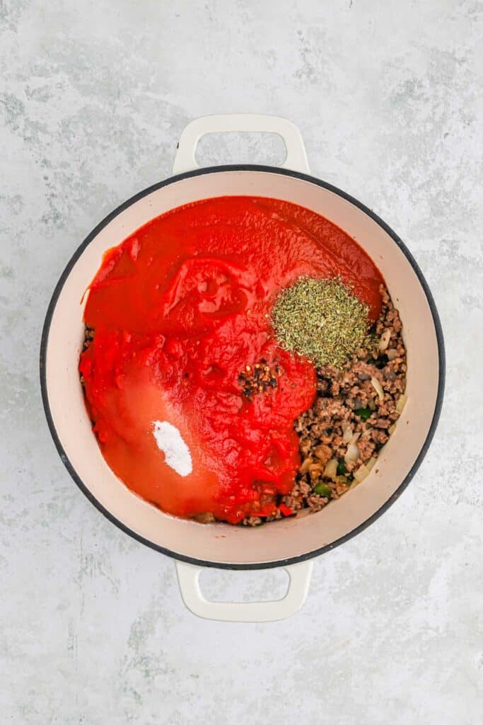 spaghetti sauce ingredients added to the meat in a pot on gray background
