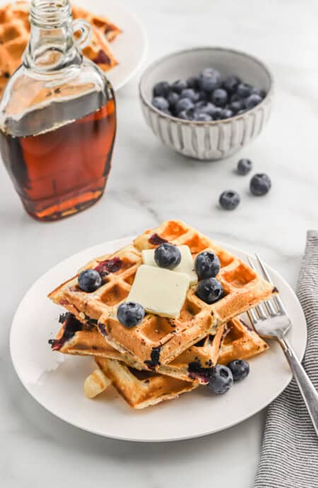 three blueberry buttermilk waffles on a plate topped with fresh berries and butter