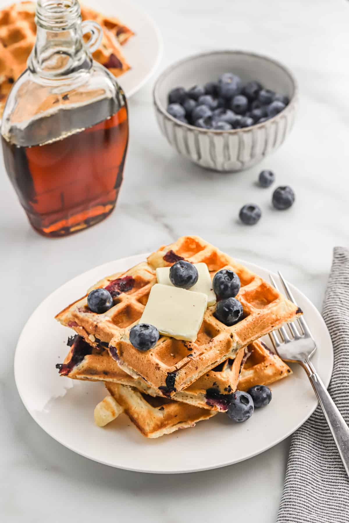 three blueberry buttermilk waffles on a plate topped with fresh berries and butter