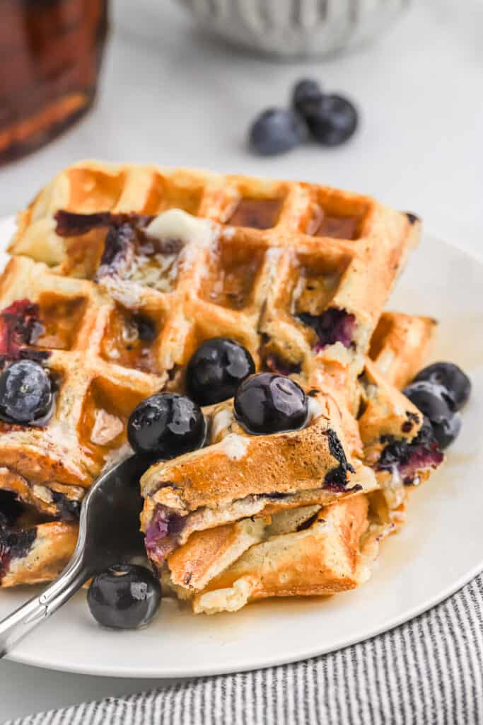 a fork cutting into the stack of blueberry waffles