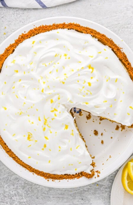 A lemon meringue icebox pie in a white pie plate with a slice missing.