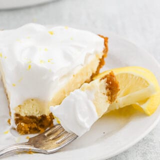 A fork with a bite of lemon icebox pie next to the slice on a plate.
