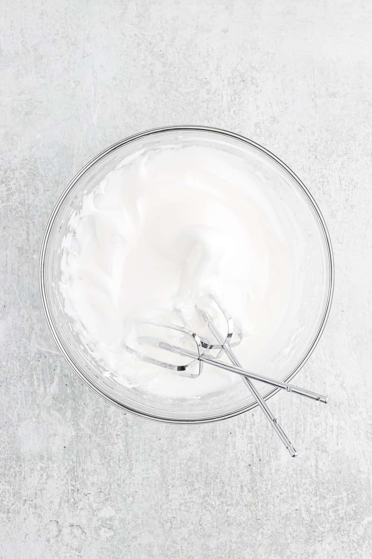 Egg whites whipped into a meringue in a glass mixing bowl.