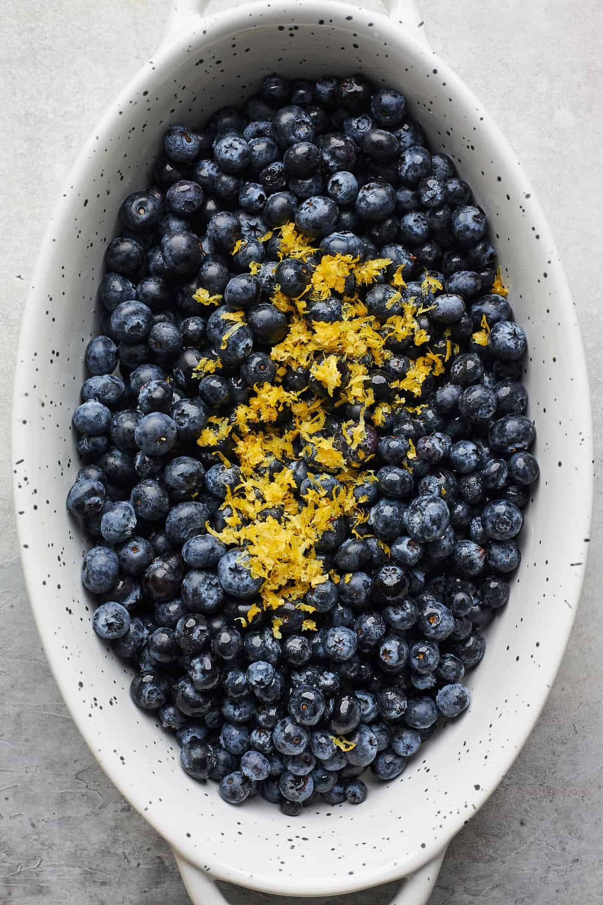 Blueberries with fresh lemon zest in an oval baking dish.