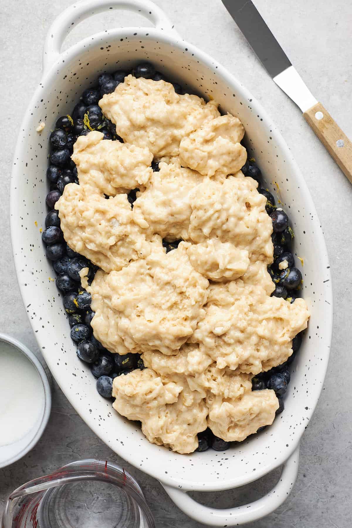 Biscuit dough spread over blueberries in an oval baking dish.