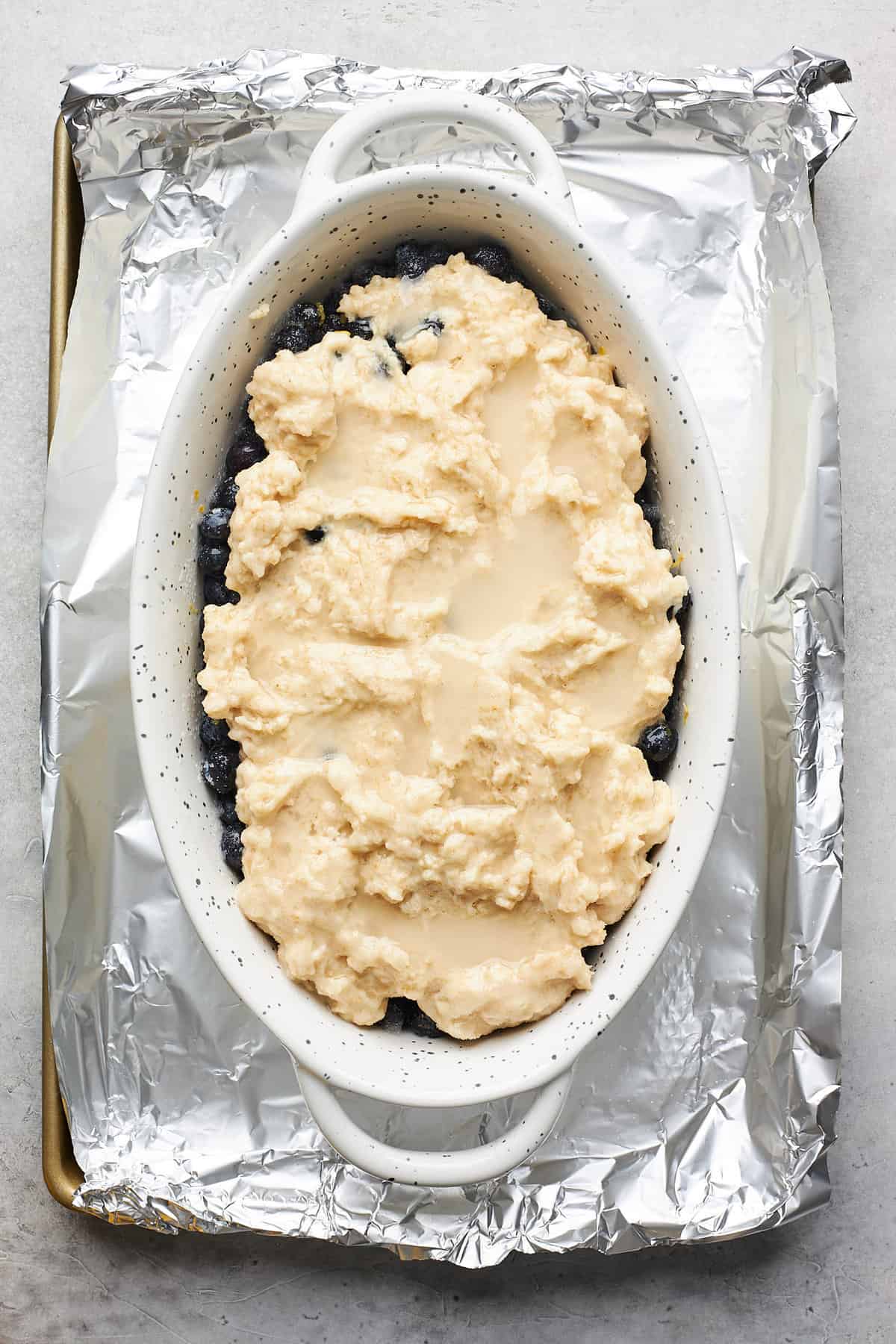 Biscuit dough spread over blueberries in an oval baking dish.