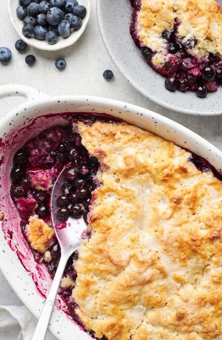 A serving spoon in a baking dish of fresh blueberry cobbler.