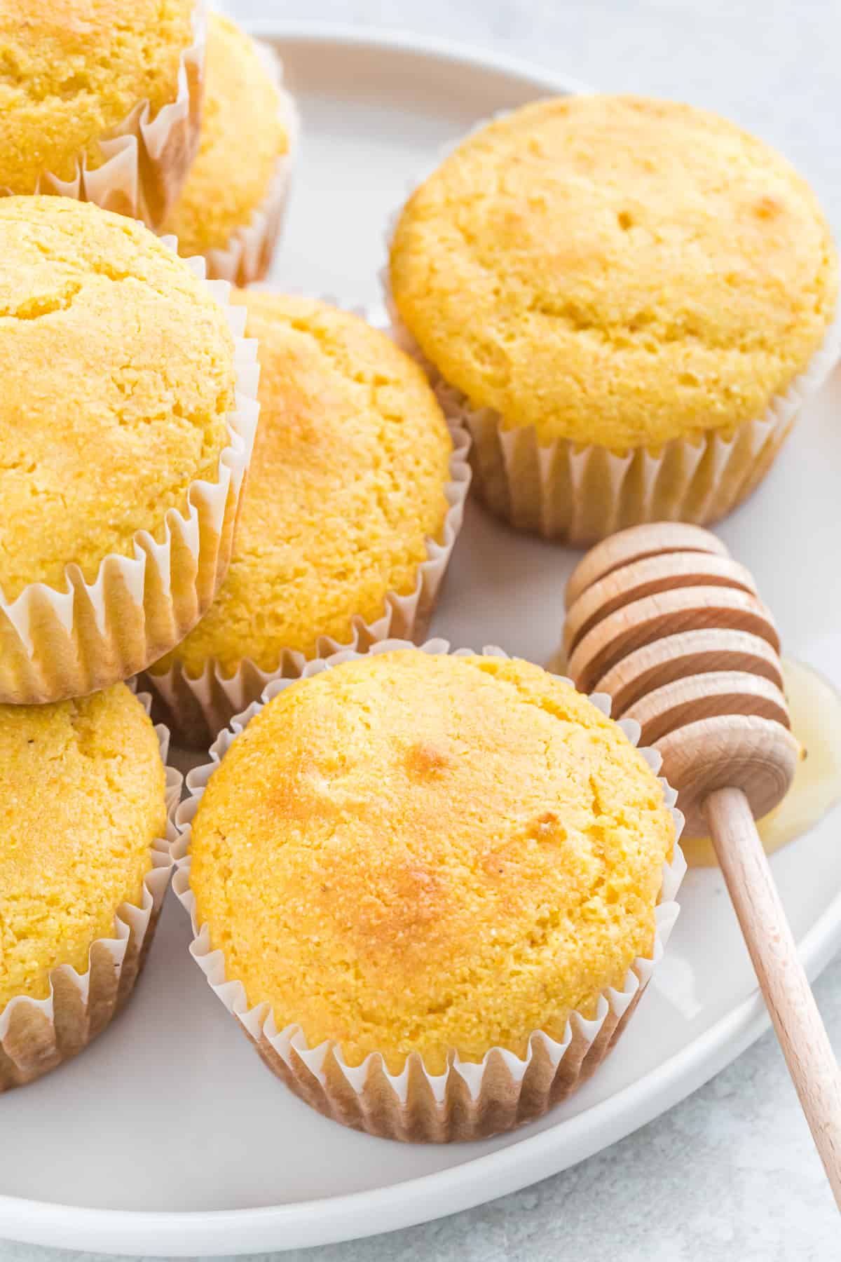 Copycat jiffy cornbread recipe as muffins stacked on a white plate with a honey dipper on the plate