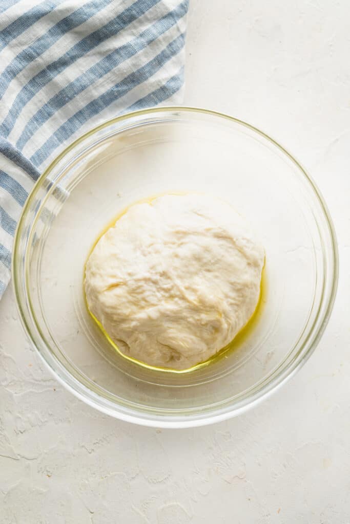 A ball of pizza dough with oil in a glass mixing bowl.
