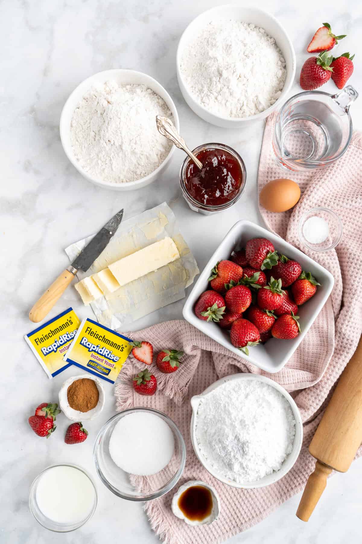 Ingredients to make strawberry cinnamon rolls in bowls on a white surface.