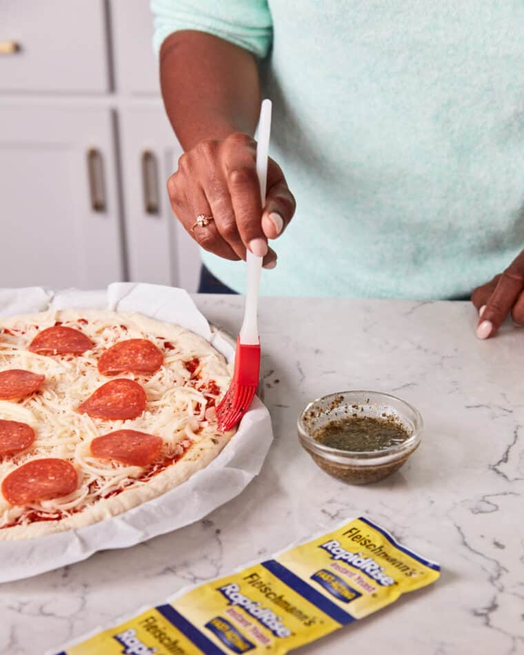Woman brushing garlic herb butter on a homemade pizza crust.
