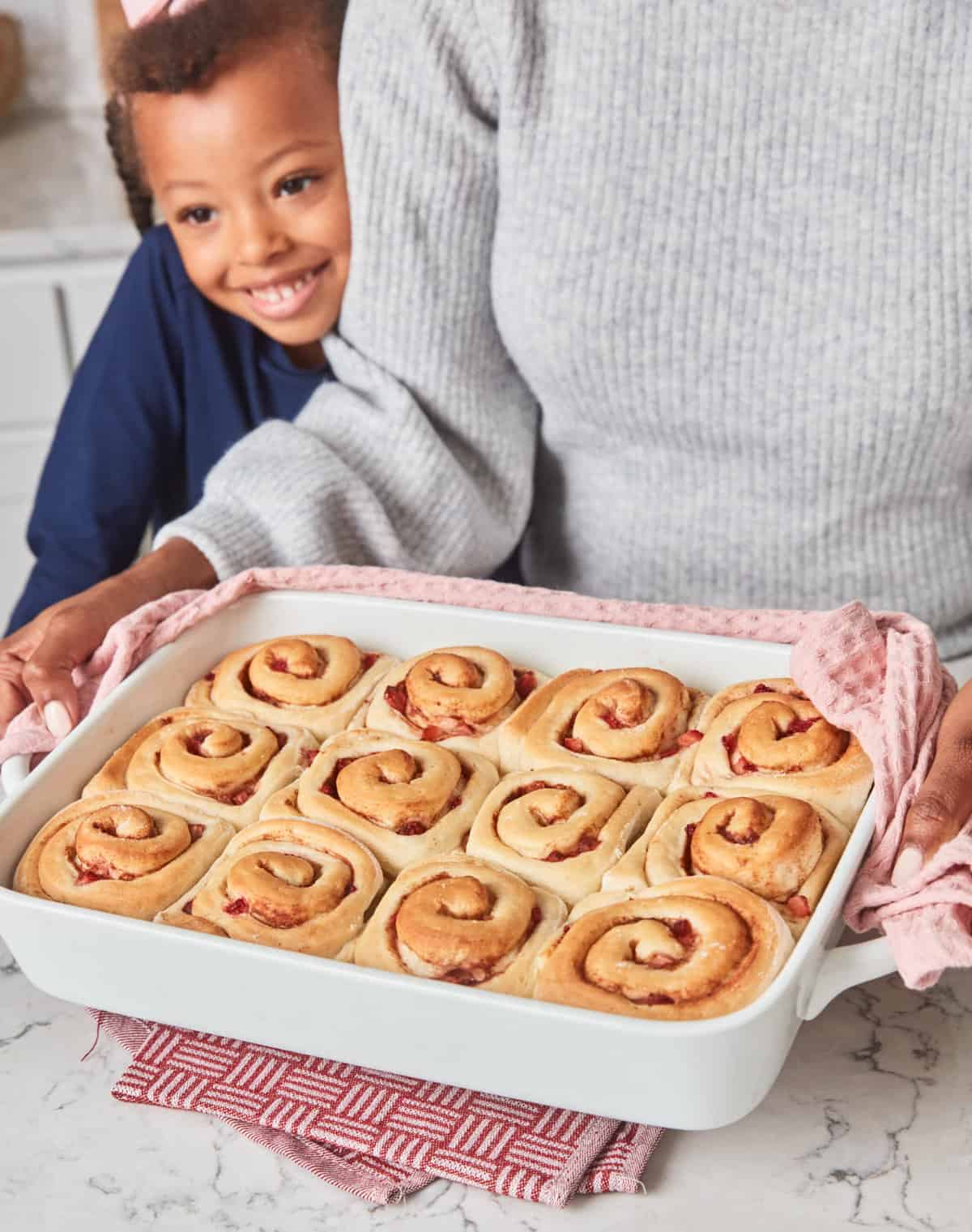 Daughter looking at a pan of cinnamon rolls in a white dish.