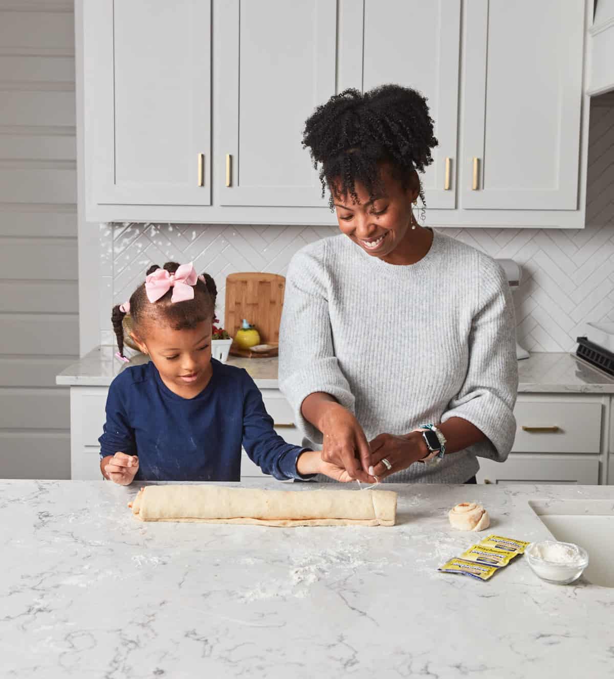 Mom and daughter slicing a roll of dough.