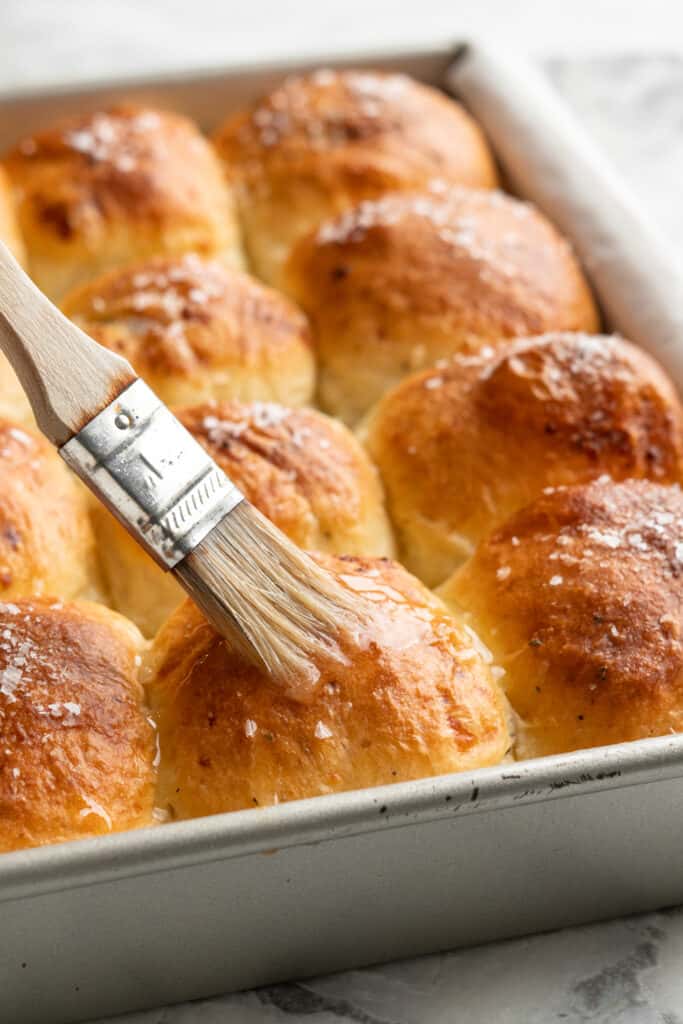 Butter being brushed over fresh baked rolls.