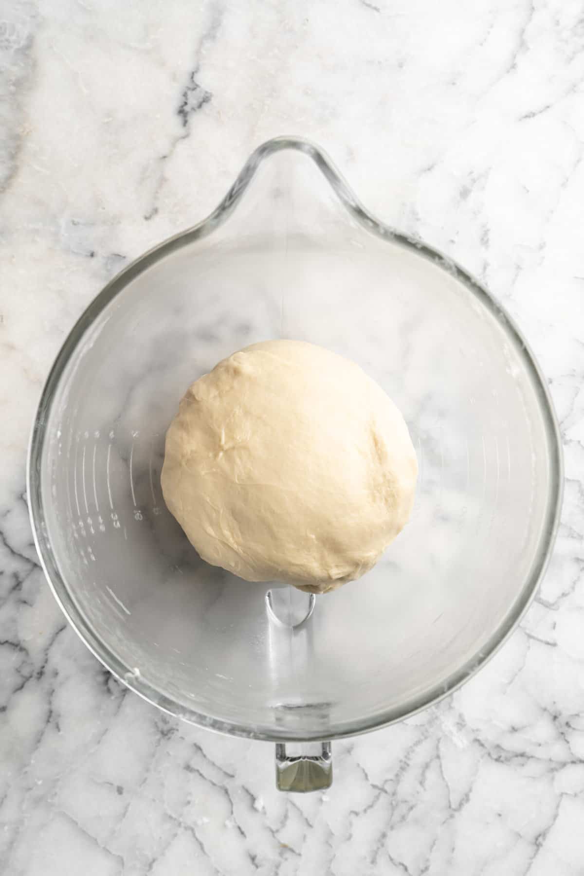 A ball of rosemary cheddar dough proofing in a glass bowl.