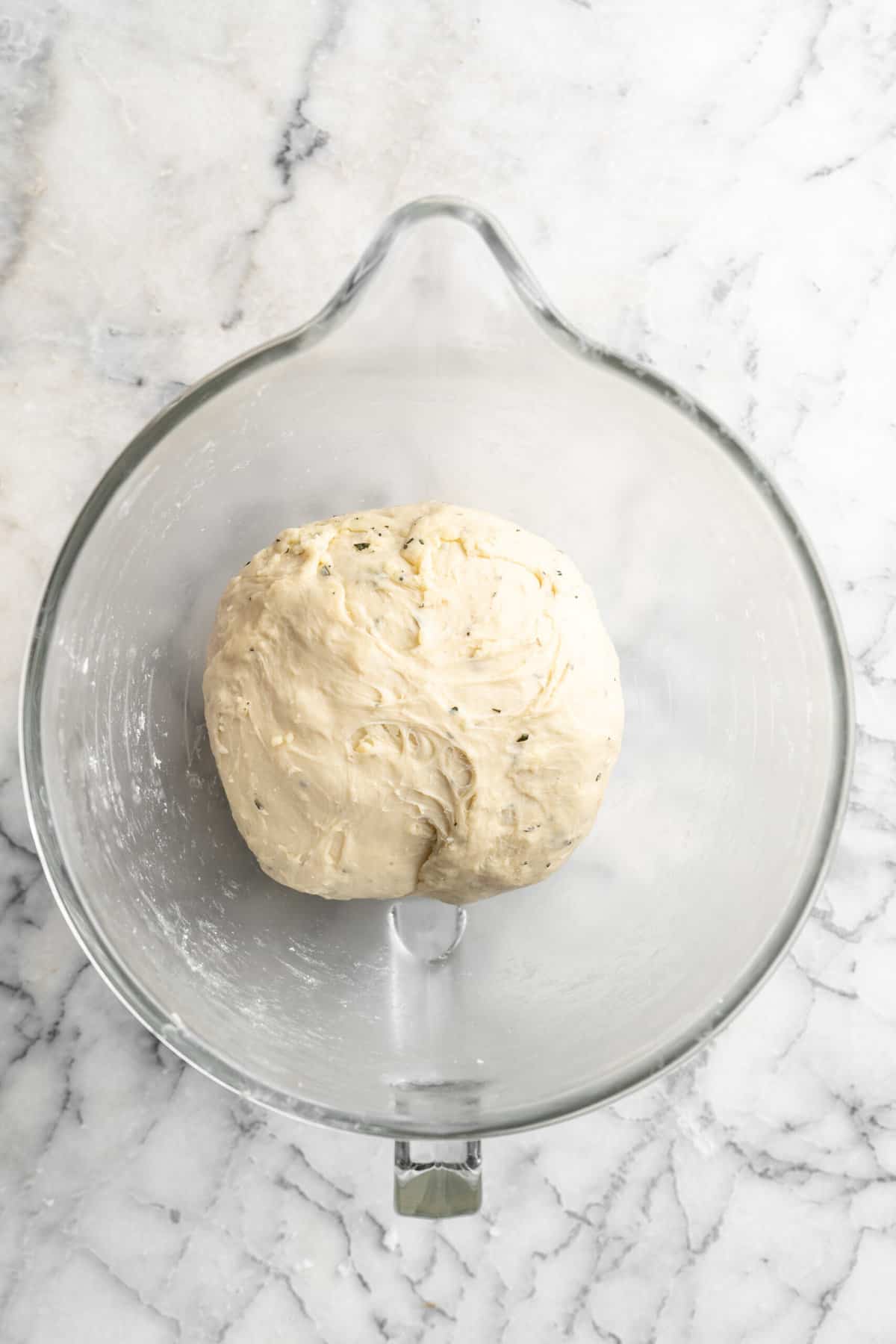 A ball of rosemary cheddar dough proofing in a glass bowl.