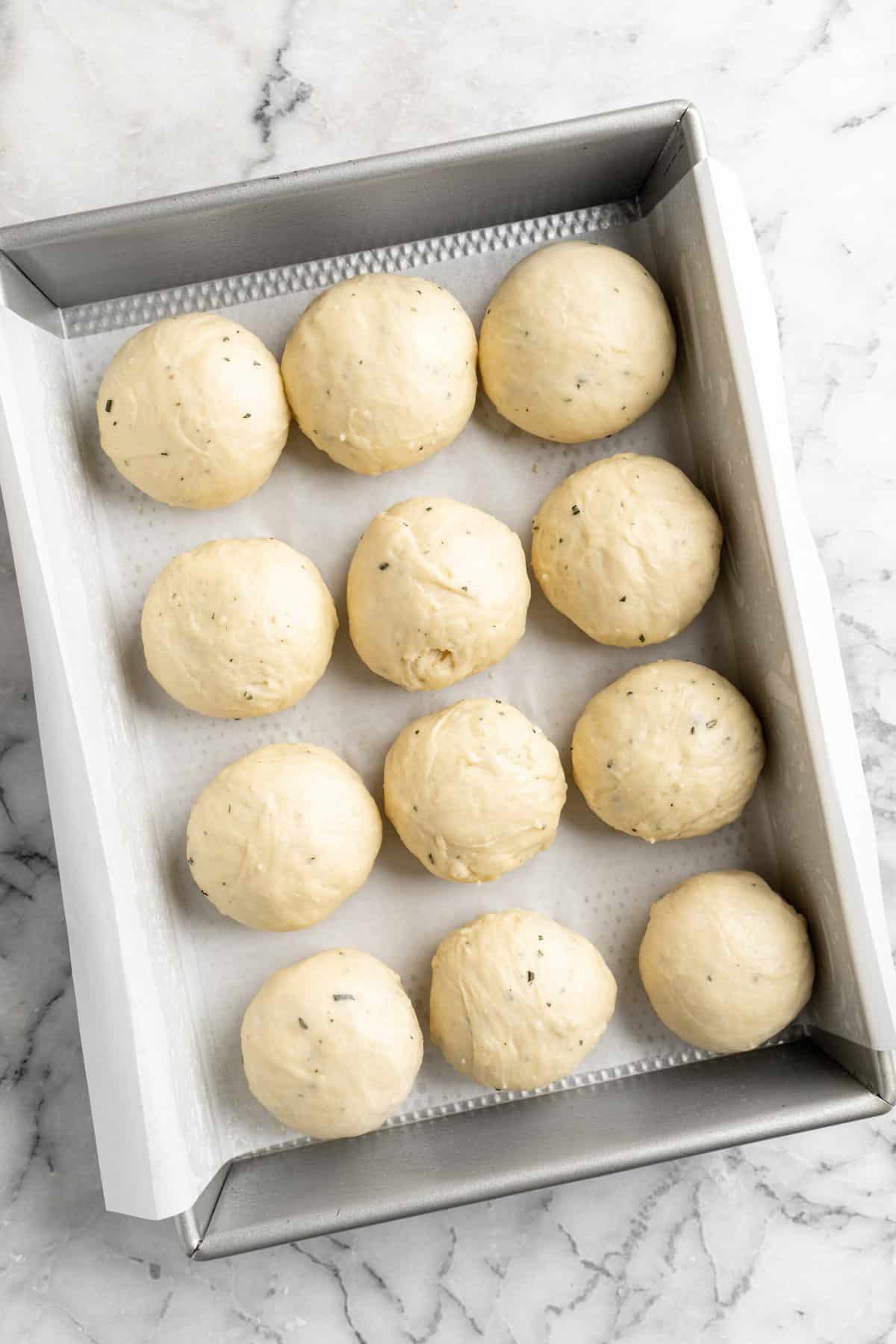 Rosemary white cheddar rolls proofing in a rectangle baking pan.