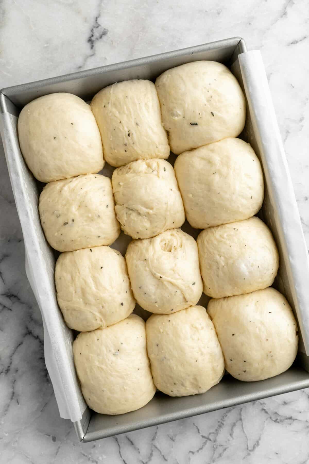 Rosemary white cheddar rolls proofing in a rectangle baking pan.