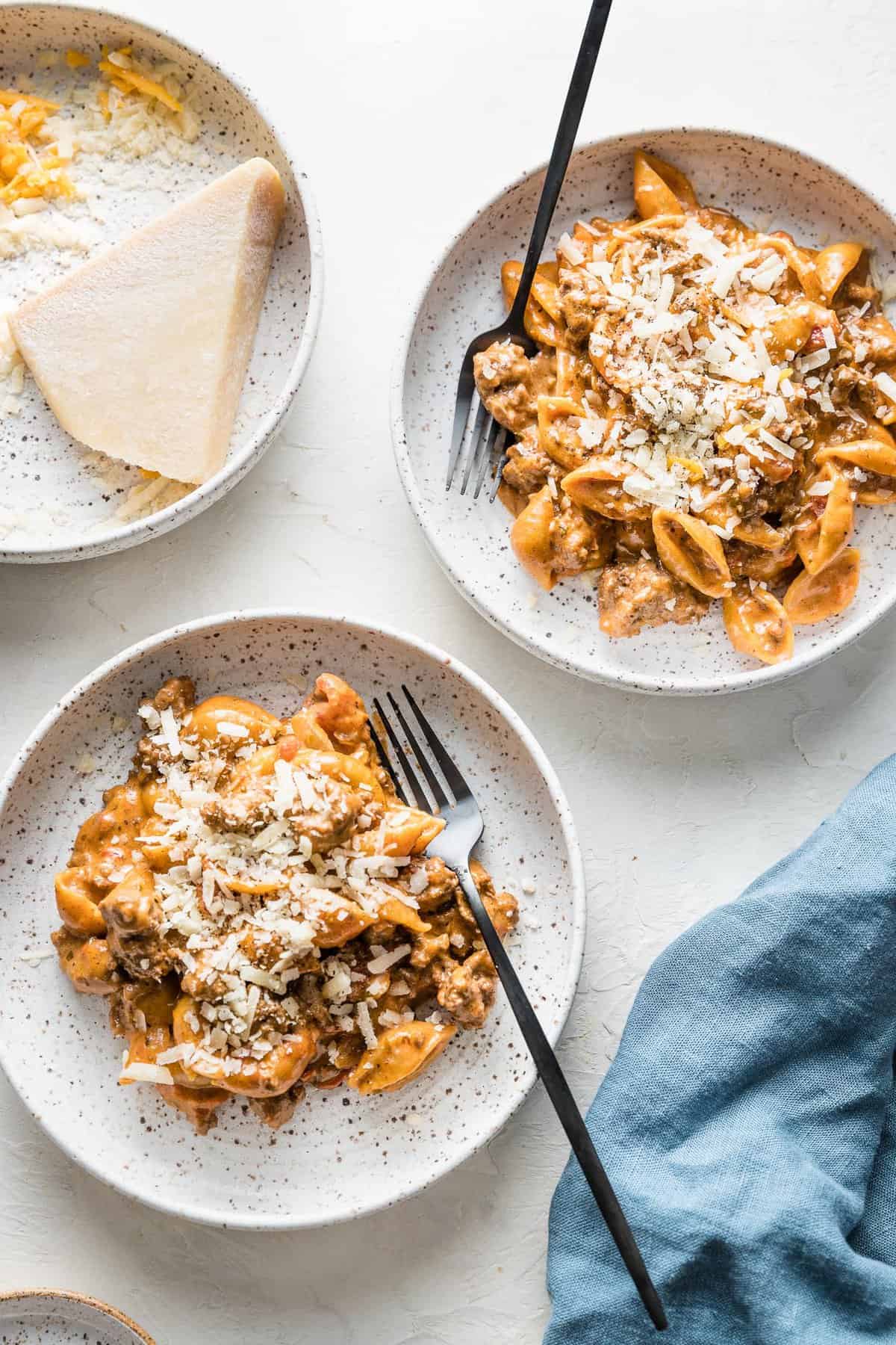 two plates of hamburger helper recipe topped with cheese on a white background