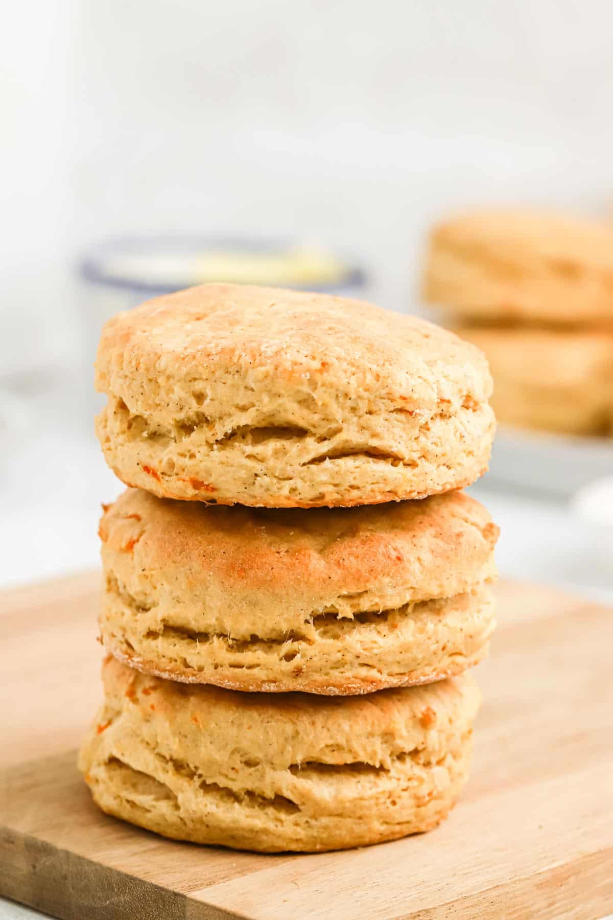 Three sweet potato biscuits stacked on a cutting board with more in background.