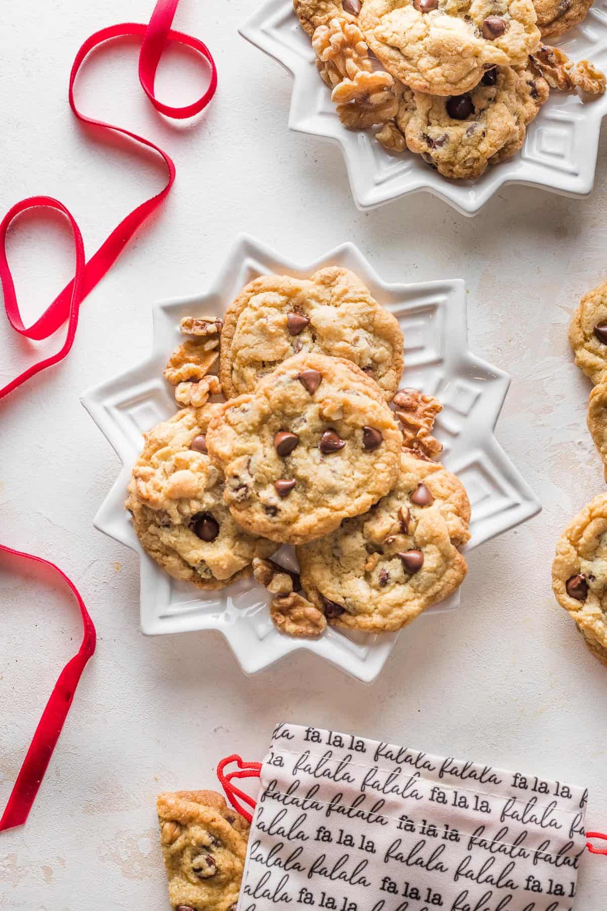 Walnut chocolate chip cookies stacked on white star-shaped plates with red ribbon and holiday napkin nearby