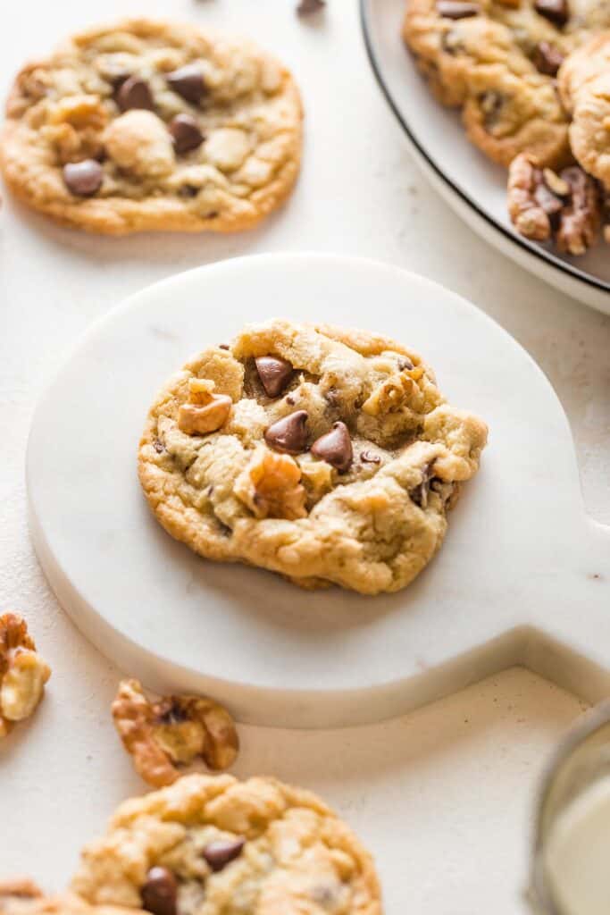 A single walnut chocolate chip cookie on a marble platter