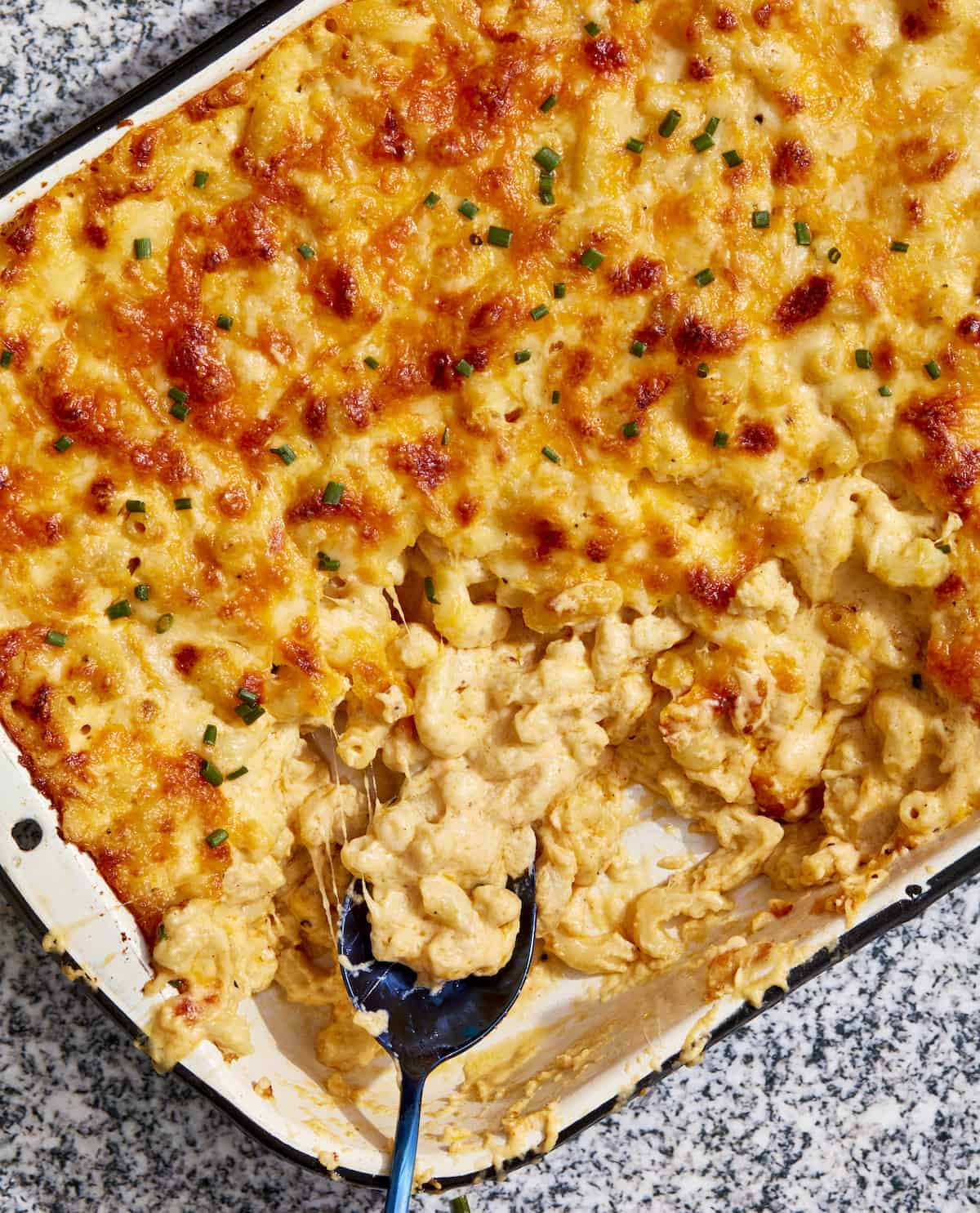 A serving spoon in a large baking dish of macaroni and cheese.