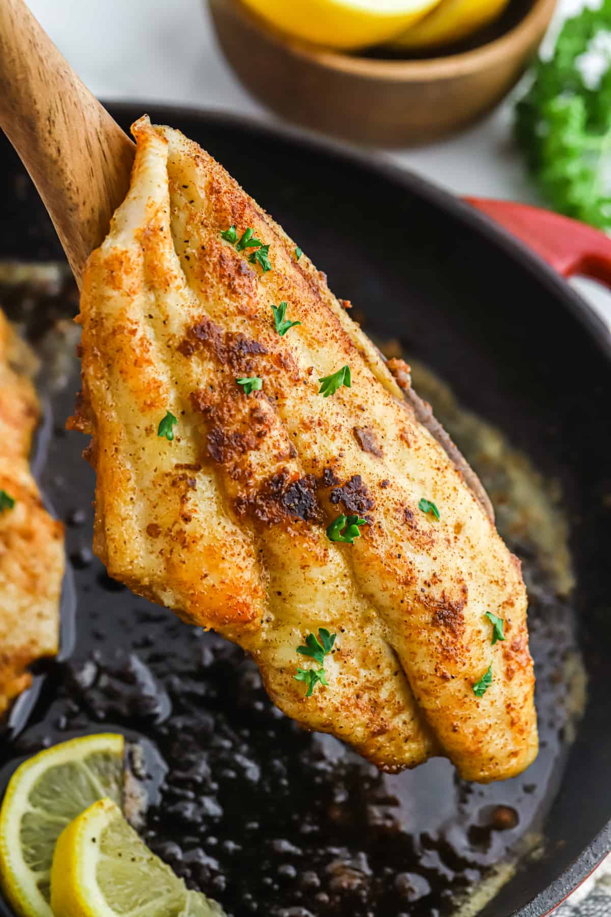 A wooden spatula with a blackened catfish fillet over a cast iron pan.