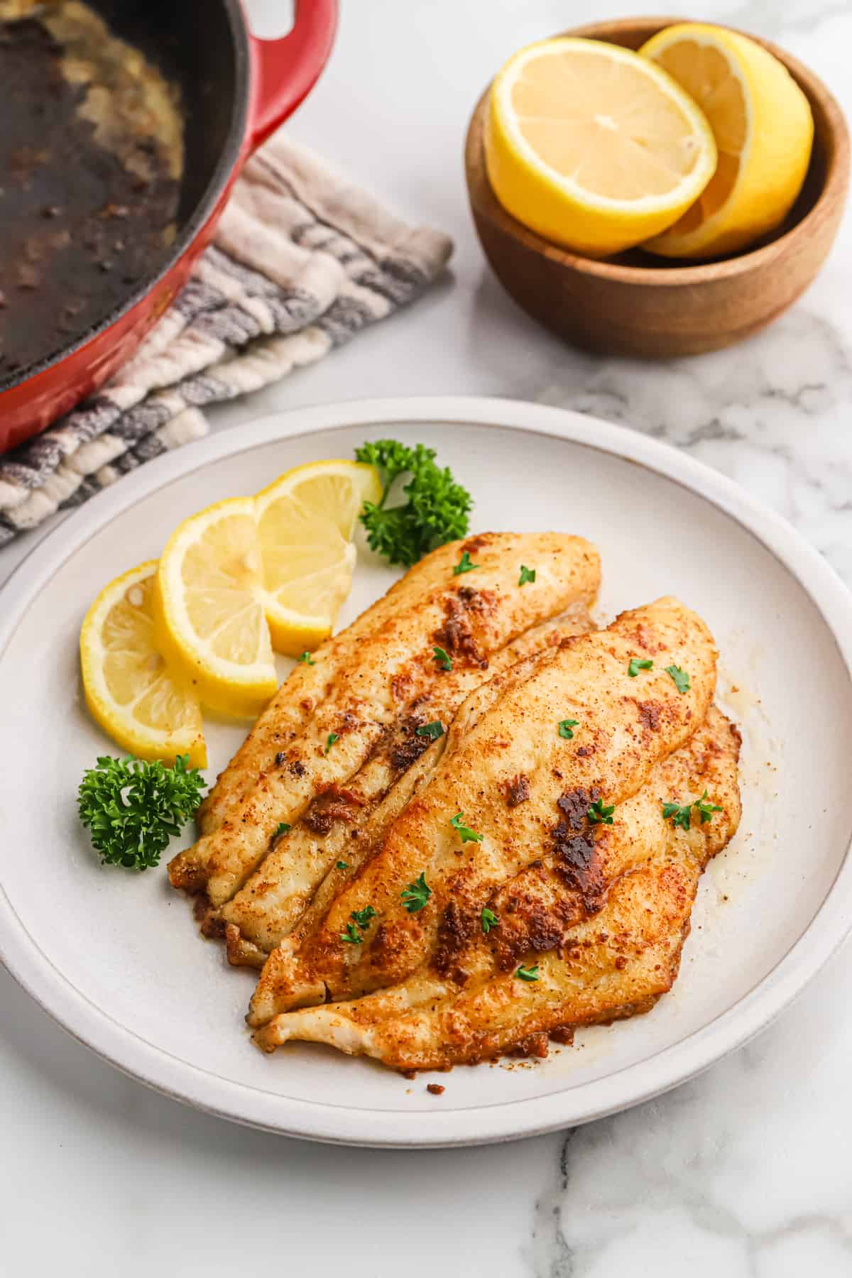 Blackened catfish fillets on a plate with lemon slices.