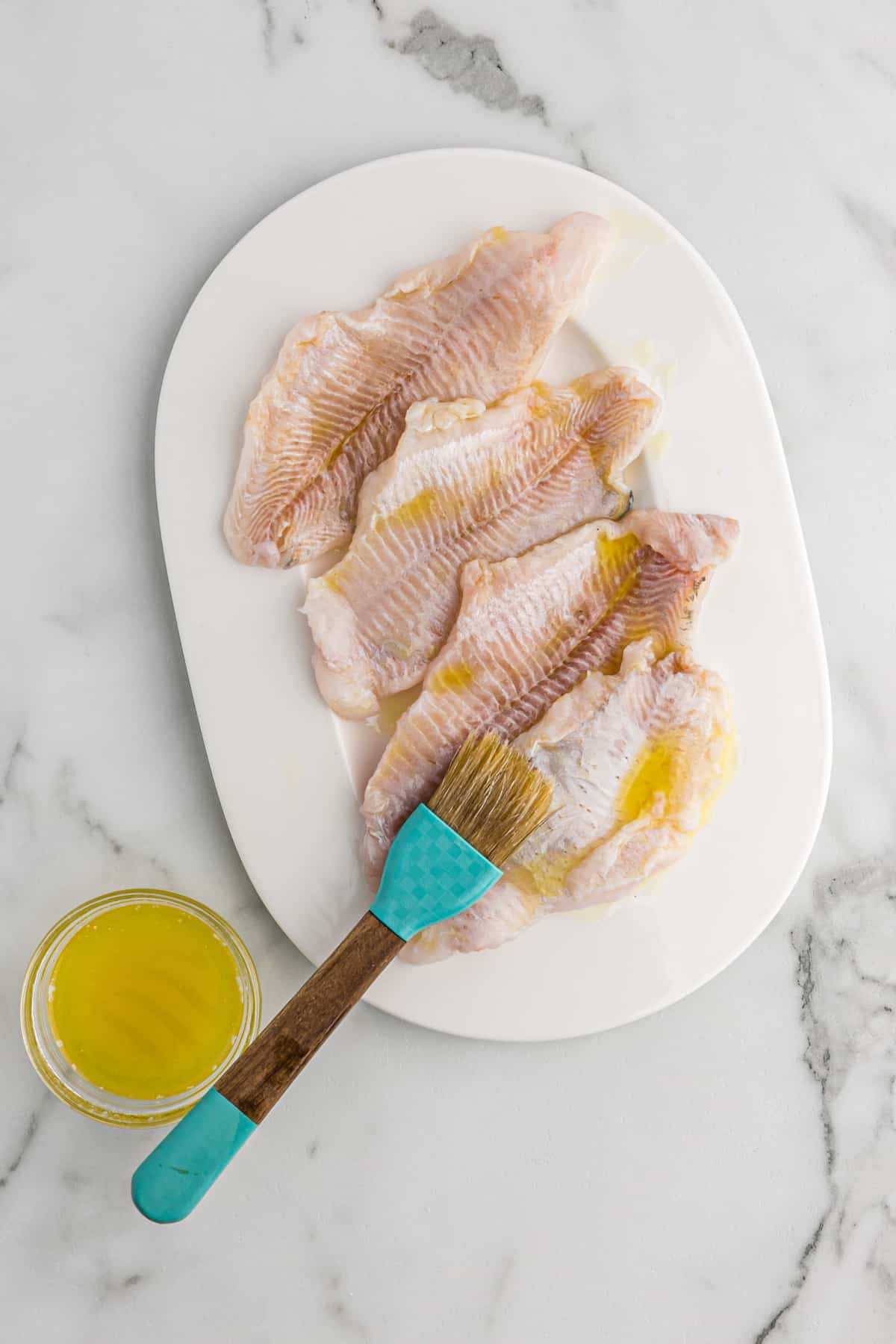 Melted butter being brushed on catfish fillets on a platter.