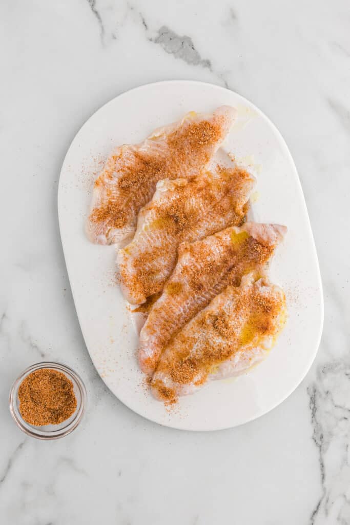 Raw seasoned catfish fillets on a white platter.