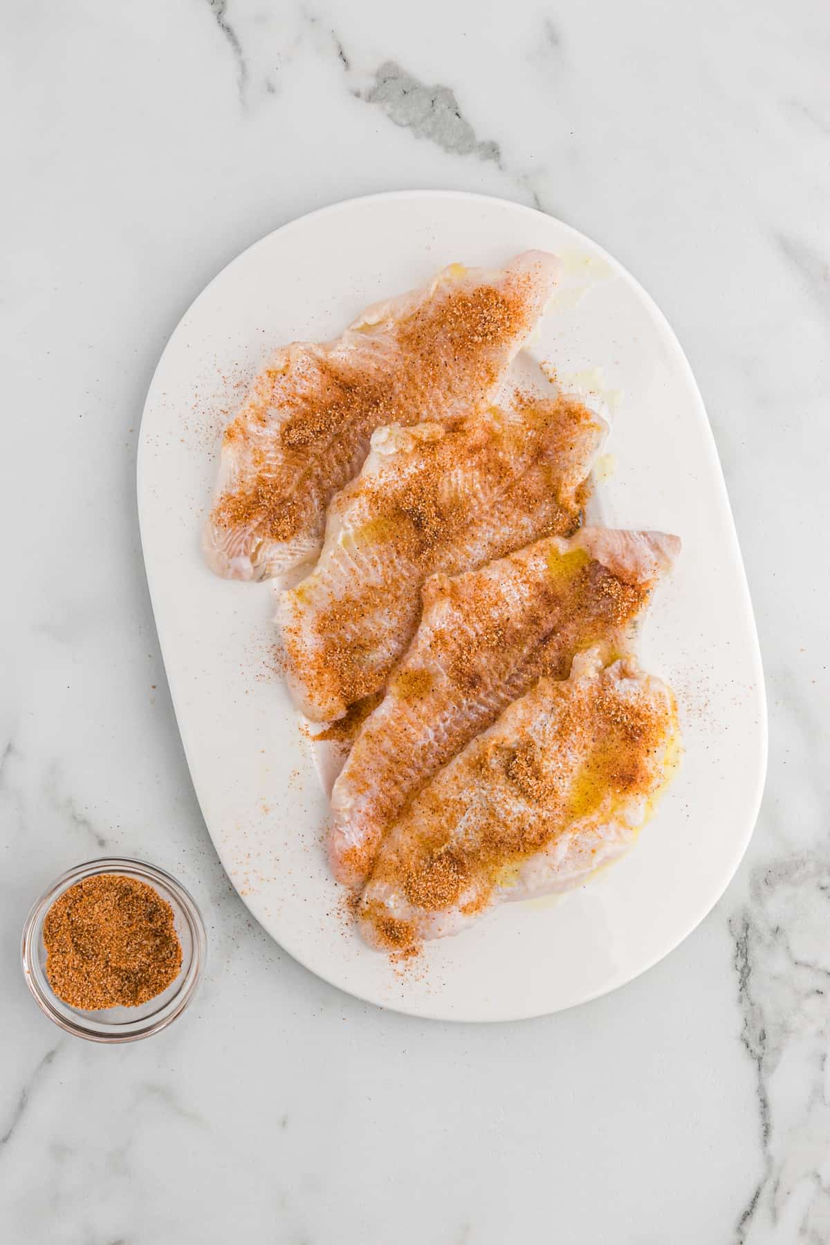 Raw seasoned catfish fillets on a white platter.