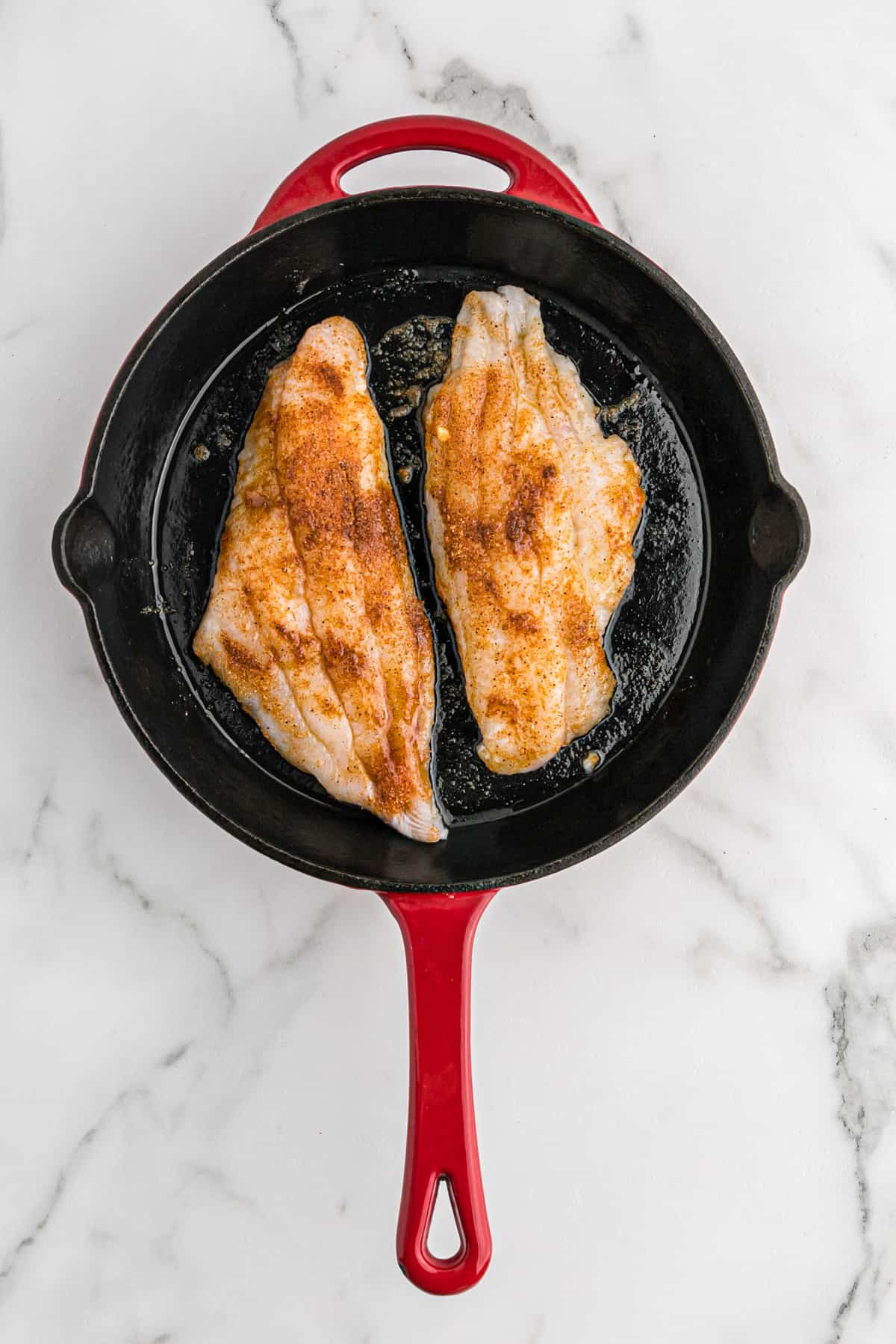 Seasoned catfish fillets in a hot cast iron skillet.