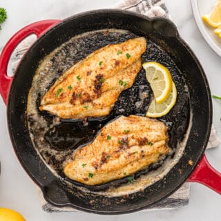 Blackened catfish filets in a red cast iron skillet.