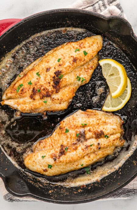 Blackened catfish filets in a red cast iron skillet.