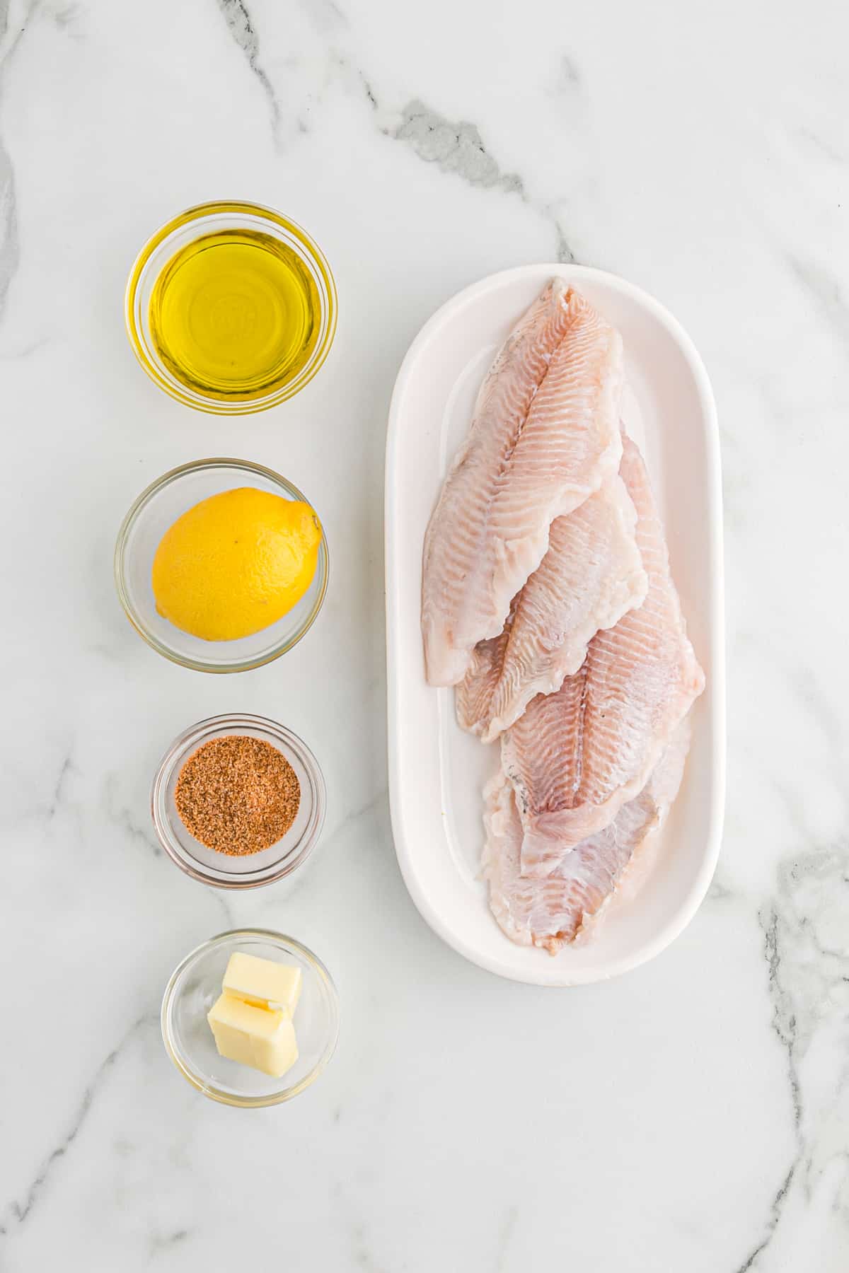 Catfish fillets on a plate with marinade ingredients in small bowls.