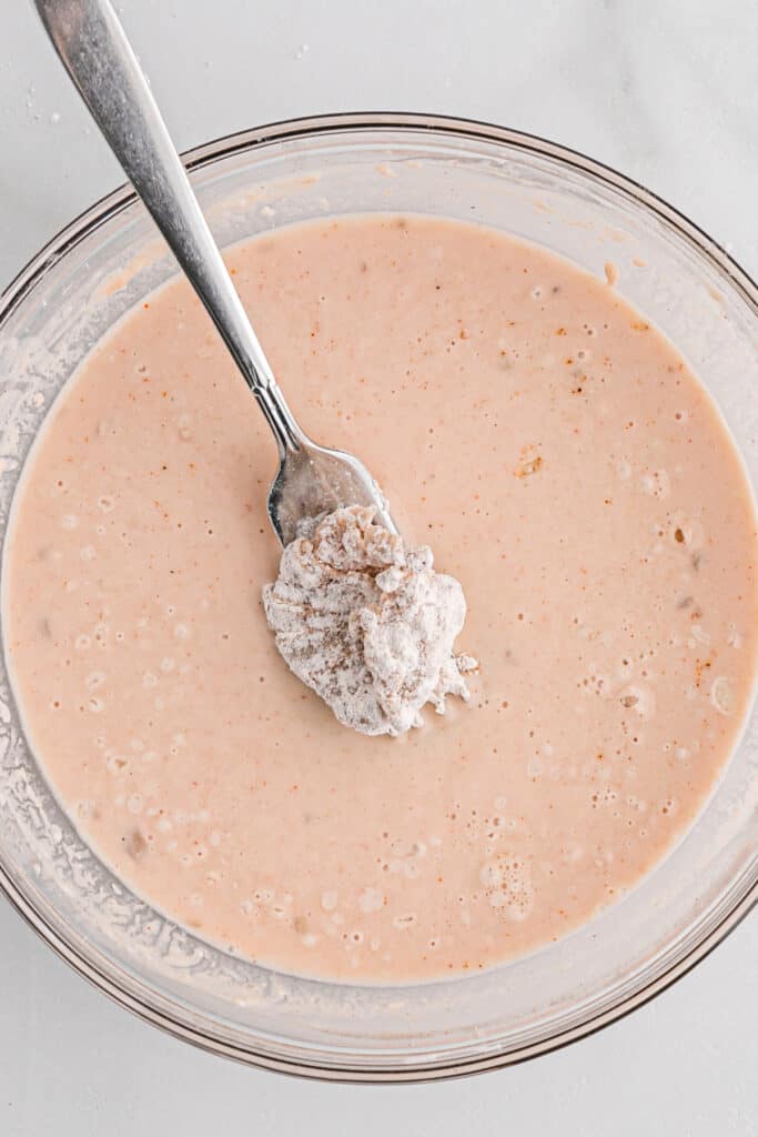 A fork placing a dredged oyster mushroom into a bowl of batter.