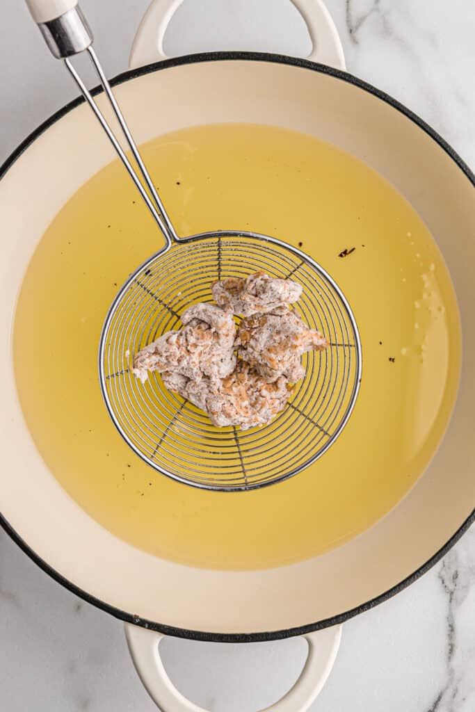 A metal spider placing battered oyster mushrooms into oil.