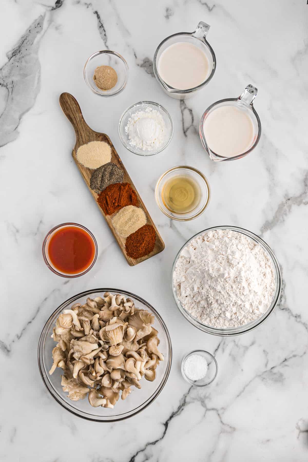 Ingredients to make battered and fried oyster mushrooms in small bowls on a white surface.