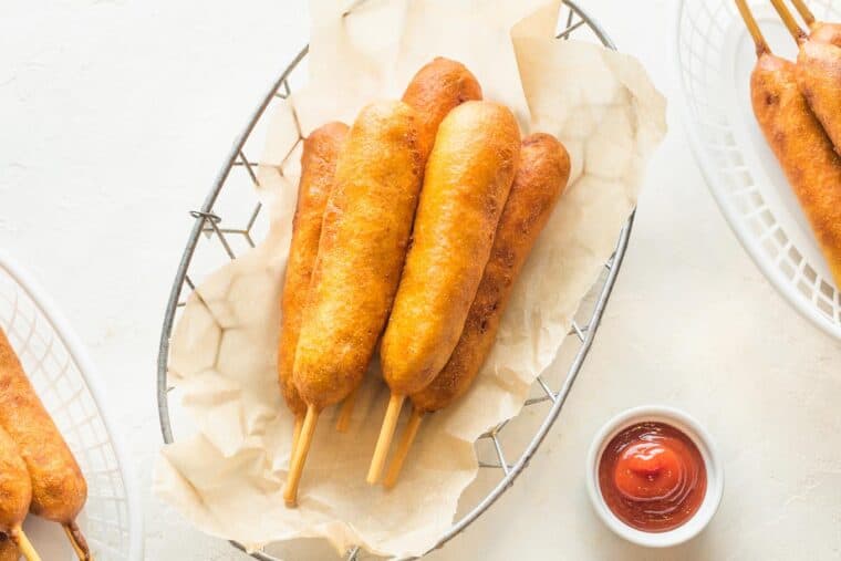 A basket of corndogs with ketchup and mustard sauce cups.