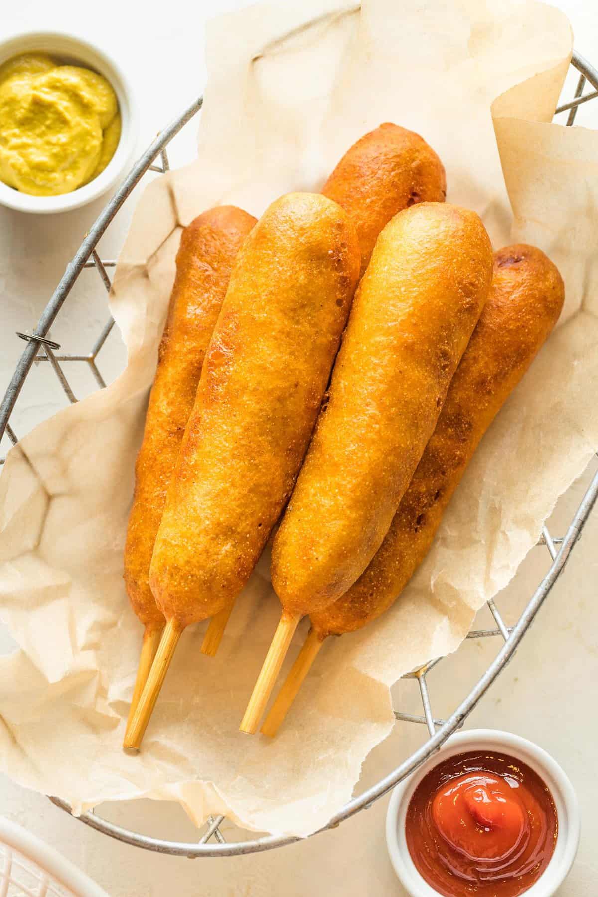 A basket of corndogs with ketchup and mustard sauce cups.
