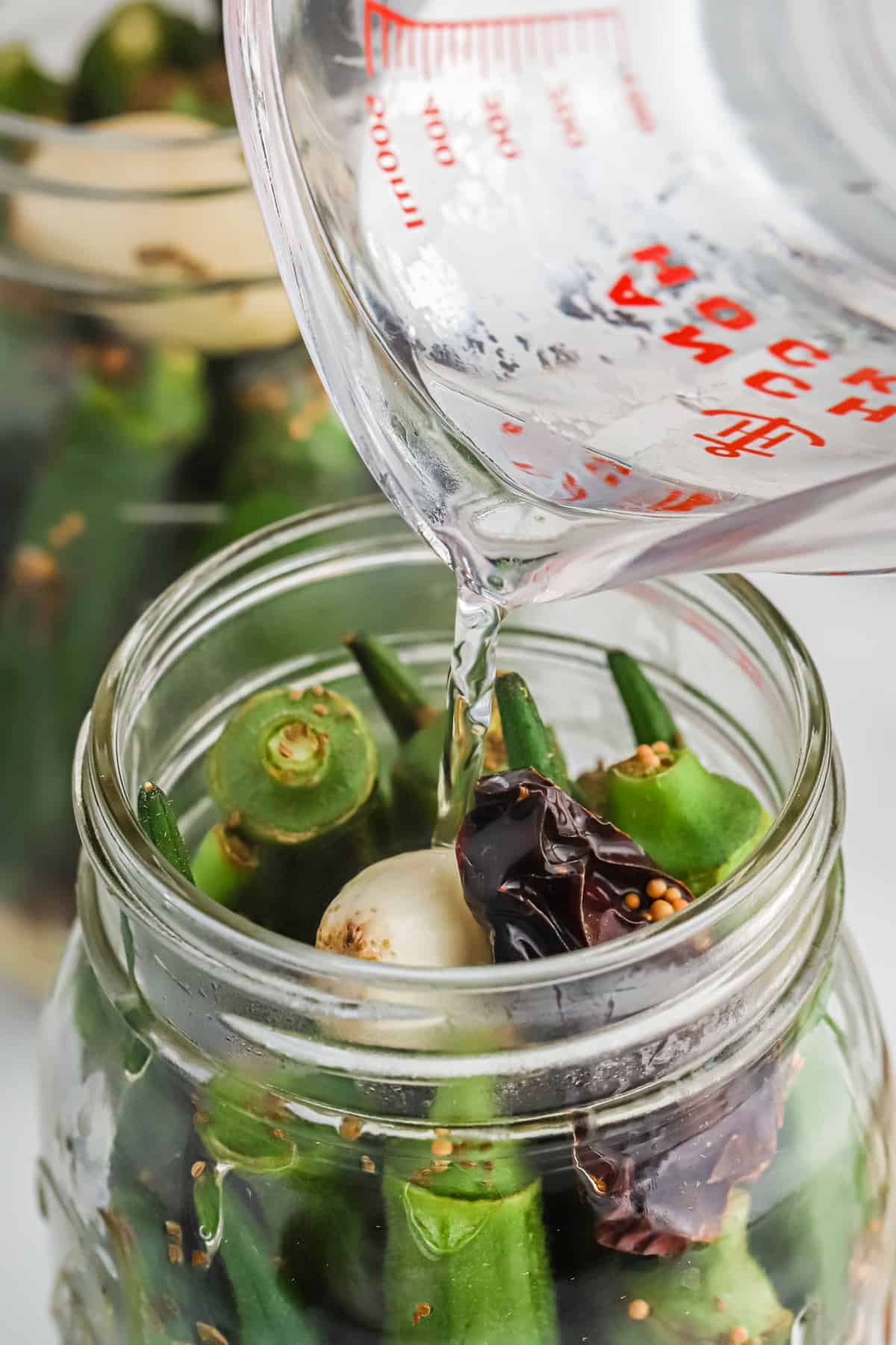 Water and vinegar mixture being poured into the jar of okra.