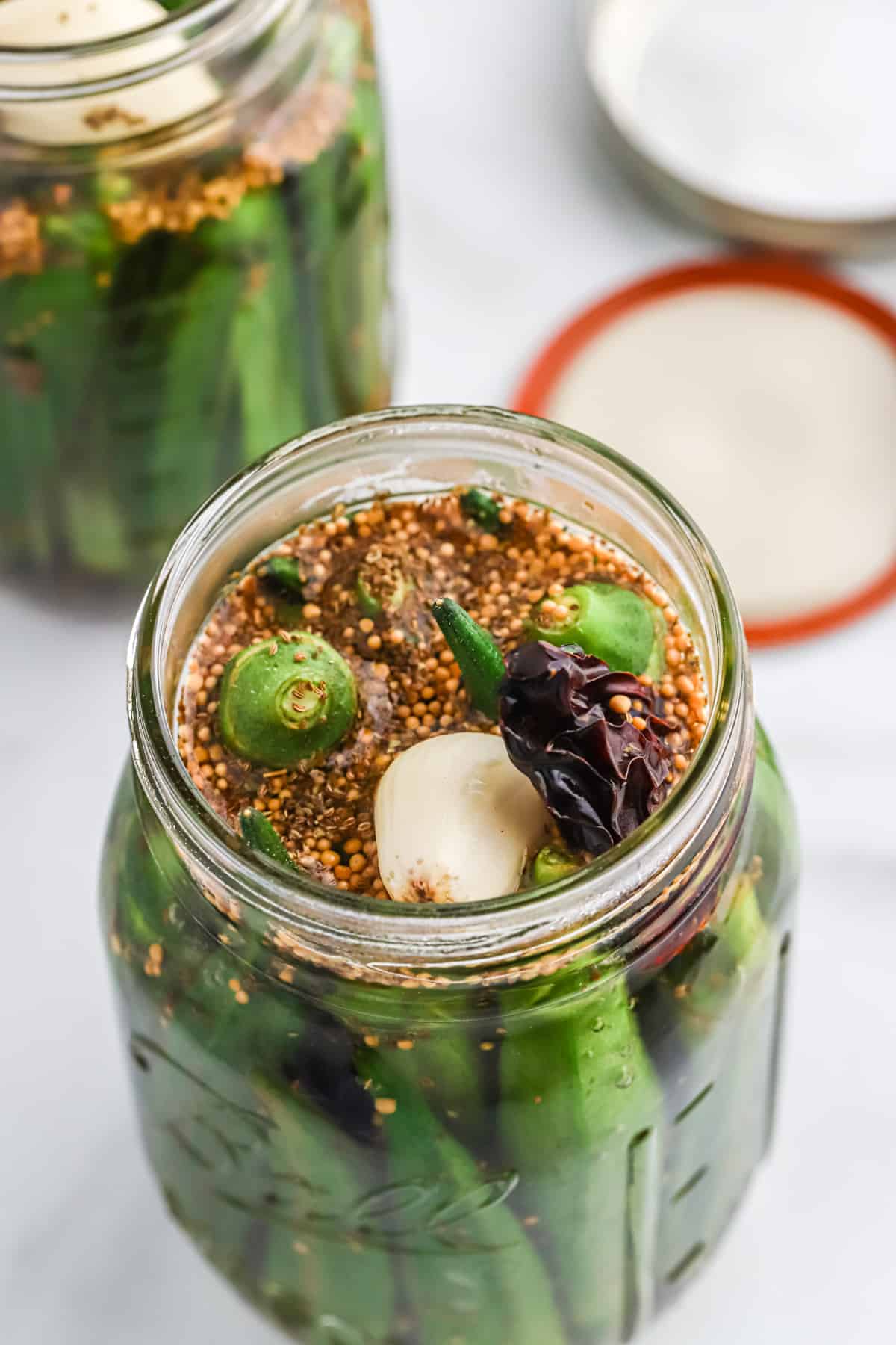 Okra packed into a jar with the spices being added.