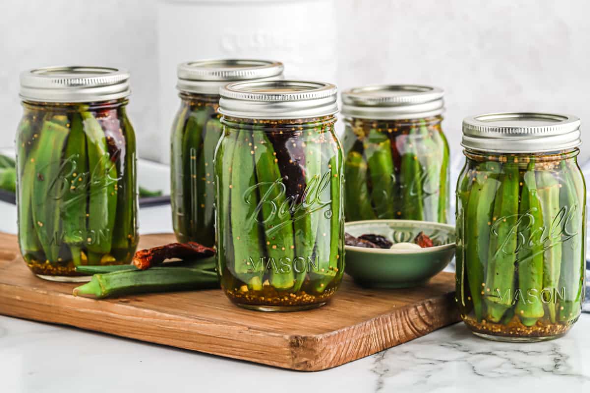 Several jars of the best pickled okra recipe on a wooden cutting board ready to open