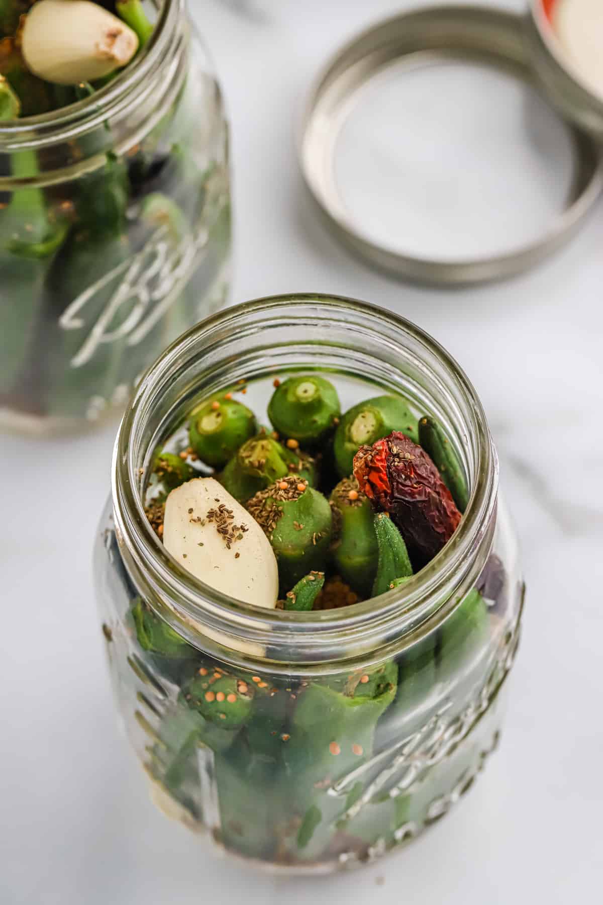 Okra packed into a jar with the spices being added.