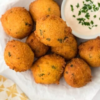 The best hush puppies fried on a paper towel with sauce in a white ramekin on a white background with yellow and white towel