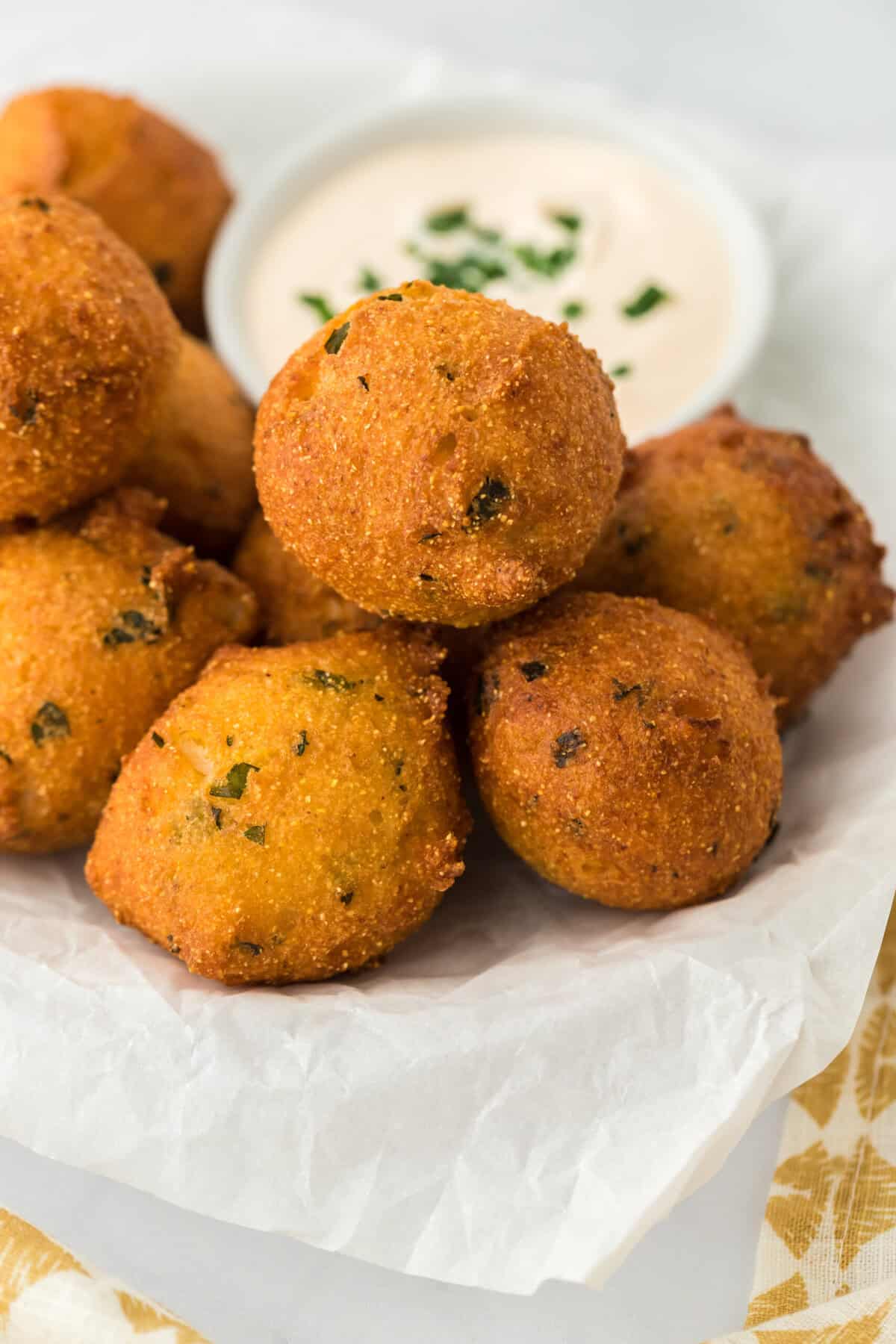 Hushpuppies pilled up on a paper towel drained with tartar sauce in a white bowl