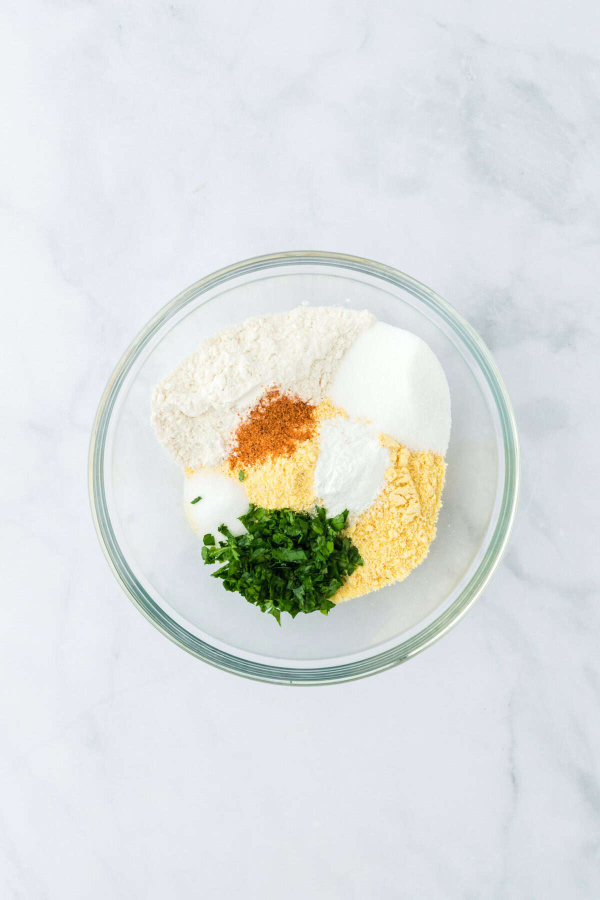 Dry ingredients added to a clear mixing bowl on a white background